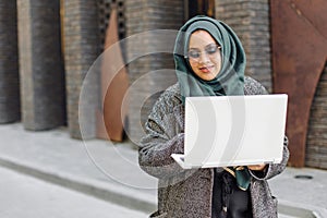 Portrait of a muslim girl in a green hijab with a laptop on the street