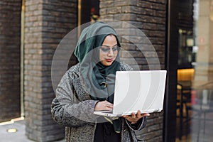 Portrait of a muslim girl in a green hijab with a laptop on the street