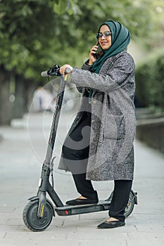 Portrait of a muslim girl in a green hijab with a scooter on the street