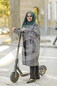 Portrait of a muslim girl in a green hijab with a scooter on the street