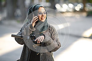 Portrait of a muslim girl in a green hijab with a scooter on the street