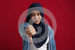 Portrait of muslim lady wearing hijab shows mocking face and thumbs down gesture, disappointed expression