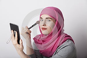 Portrait of a muslim woman wearing a head scarf and doing make-up. Isolated.