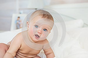 Portrait of naked smiling Infant sits on a bed in bedroom