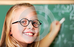 Portrait, nerd and happy kid writing on chalkboard in class for learning, education and study math. Face, glasses and