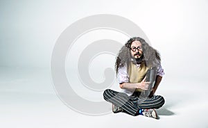 Portrait of a nerdy guy holding a briefcase and sitting on white floor