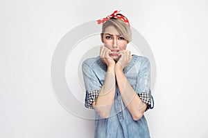 Portrait of nervous beautiful young woman in casual blue denim shirt with makeup and red headband standing looking at camera and