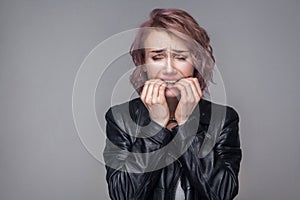 Portrait of nervous girl with short hairstyle and makeup in casual style black leather jacket standing biting her nails and