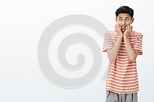 Portrait of nervous and scared young asian boy in striped t-shirt biting fingers looking at upper left corner insecure