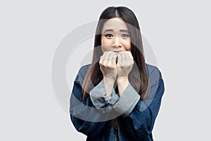 Portrait of nervous shocked beautiful brunette asian young woman in casual blue denim jacket with makeup standing bitting her nail