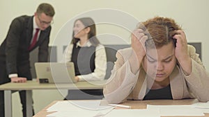 Portrait nervous woman sitting at the table in the foreground holding her head with hands, she has trouble at work