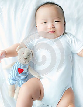 Portrait of a newborn Asian baby boy on the bed , Charming Fat baby 5 month old lies in bed and the doll ,enjoy and happy,soft and