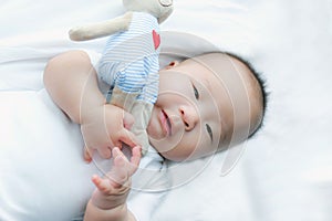 Portrait of a newborn Asian baby boy on the bed , Charming Fat baby 5 month old lies in bed and the doll ,enjoy and happy,soft and