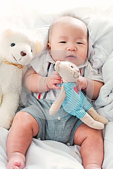 Portrait of a newborn Asian baby boy on the bed with a doll , Charming