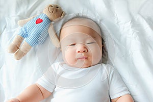 Portrait of a newborn Asian baby boy on the bed with a doll , Charming