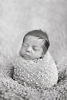 Portrait of newborn baby boy wrapped in popcorn wrap. Infant sleeping. Newborn baby with beautiful long dark hair. Black and white