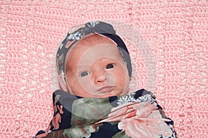 Portrait of a newborn baby girl swaddled laying on pink blanket