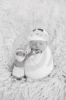 Portrait of newborn baby girl wrapped in wrap with knitted woolen crown headband. Infant on furry fluffy background