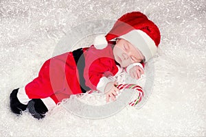 Portrait of newborn baby in Santa clothes lying under Christmas tree.