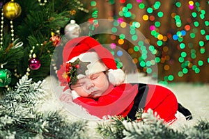 Portrait of newborn baby in Santa clothes lying under Christmas tree.