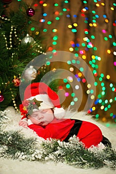 Portrait of newborn baby in Santa clothes lying under Christmas tree.