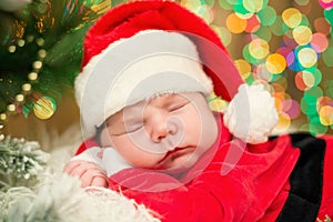 Portrait of newborn baby in Santa clothes lying under Christmas tree.