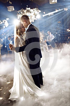 Portrait of newlyweds first wedding dance. Just married couple dancing in darkness. Groom holds bride& x27;s hand dancing