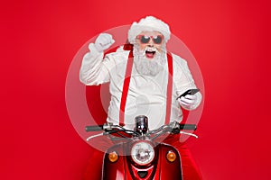 Portrait of nice attractive bearded cheerful cheery glad funny funky Santa wearing cap hat sitting on motor bike using