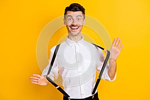 Portrait of nice attractive cheerful guy wearing white shirt pulling suspenders having fun isolated over bright yellow