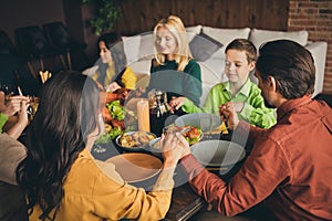 Portrait of nice attractive peaceful multi generation family sitting around served table holding hands praying eating