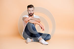 Portrait of nice attractive virile macho fit guy sitting on floor resting isolated over beige color background