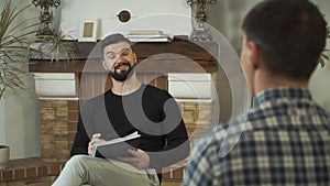 Portrait of nice Caucasian man sitting with papers, talking, smiling. Professional male psychologist telling story to