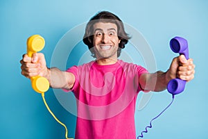 Portrait of nice cheerful guy holding in hands giving you two handsets client support isolated over bright blue color