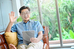 Portrait of nice cheerful positive old man sitting on divan hold