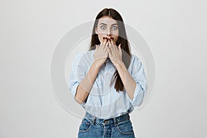 Portrait of nice and cute european student, covering mouth with hands, expressing shock and surprise with widened eyes