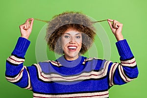 Portrait of nice girl with perming coiffure dressed knit pullover holding curls showing new hairdo isolated on green