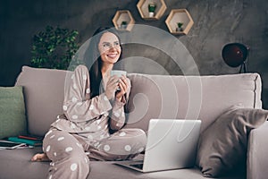 Portrait of nice optimistic girl hold cup look empty space wear spectacles pijama at home on sofa photo