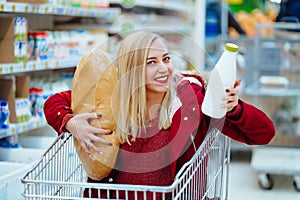 Pretty young hipster woman sitting in a supermarket trolley at the supermarket