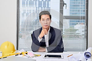 Portrait of a nice smiling man, working at home on some project, he is sitting at a white table looking at camera, writing ideas