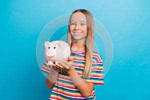 Portrait of nice teen girl with long hair wear colorful t-shirt arms hold piggy box look empty space isolated on blue