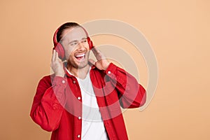 Portrait of nice young man headphones empty space wear red shirt isolated on beige color background