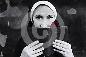 portrait of a nun in black clothes reading the bible and using a rose petal as a bookmark