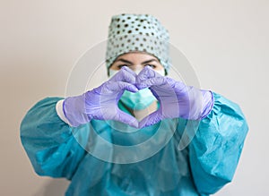 Portrait of a nurse wearing hygienic face surgical medical mask and gown showing a heart with hands