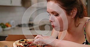 Portrait of the obese woman quickly eating tasty pizza at the kitchen.