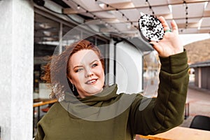 Portrait of a obesed smiling woman holds a chocolate donut and looking at it. The concept of diet and obesity