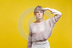 Portrait of observant beautiful young woman with fair hair in casual beige blouse, isolated on yellow background