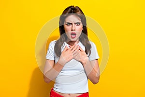 Portrait of offended abused girl red lips wear white t-shirt hold hands on chest astonished staring isolated on yellow