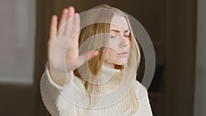 Portrait of offended blonde caucasian woman makes stop gesture with her palm forbidding waving head no. Young girl in