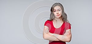 Portrait of offended woman standing with arms crossed on gray background. Place for your text