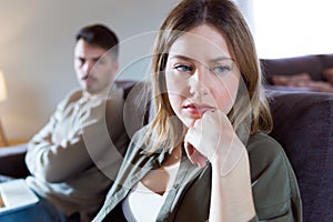 Offended young woman ignoring her angry partner sitting behind her on the couch at home. photo